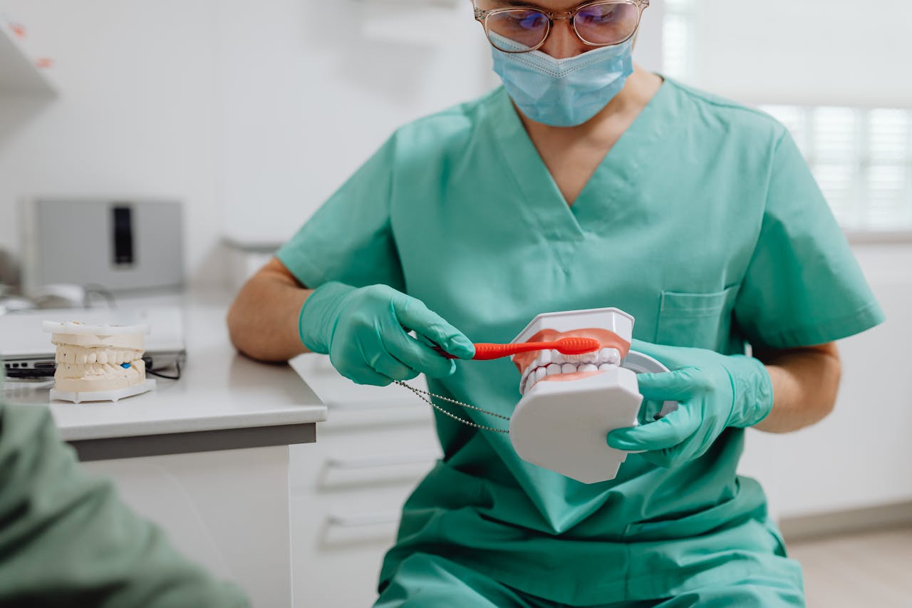 our-story-01 Dental professional in scrubs demonstrates proper brushing on a model in a clinic setting.